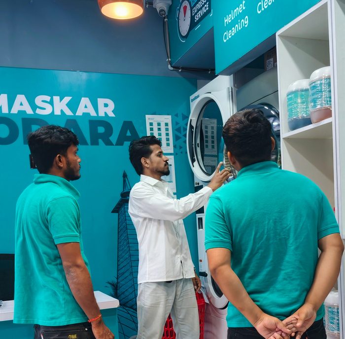 Trainer demonstrating a commercial washing machine to two trainees